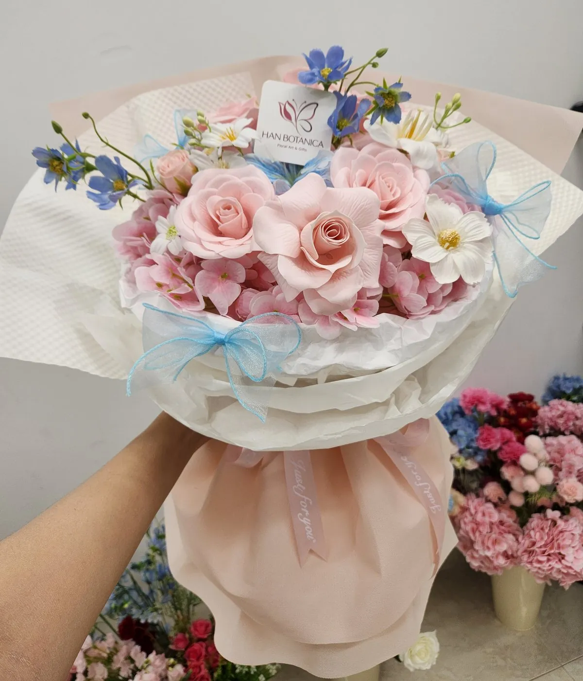 Bó hoa hồng phấn gói giấy trắng, thắt nơ xanh của Han Botanica